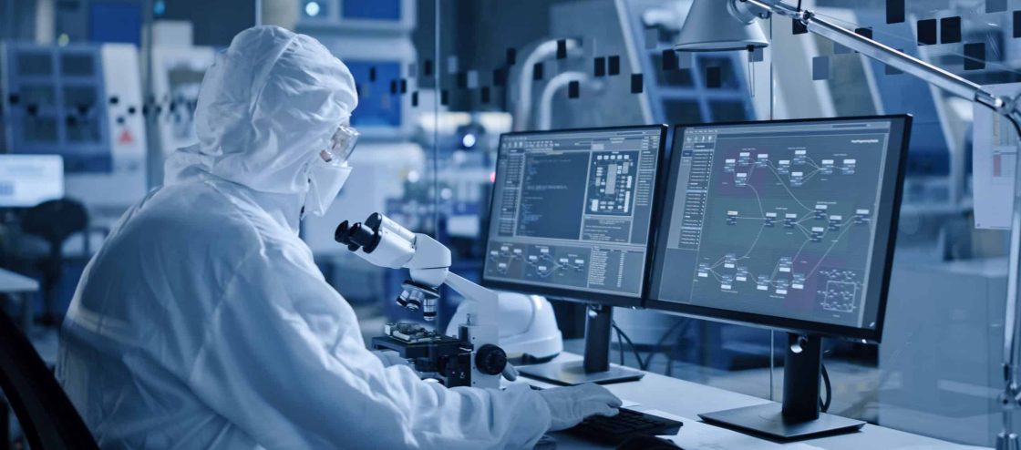 Electronics Factory Cleanroom: Engineer / Scientist in Coveralls Works on Computer, Screen Shows Infographics and Software System Control UI, Developing Electronics for Medical Electronics